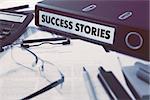 Success Stories - Office Folder on Background of Working Table with Stationery, Glasses, Reports. Business Concept on Blurred Background. Toned Image.