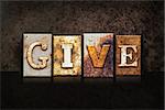 The word "GIVE" written in rusty metal letterpress type on a dark textured grunge background.