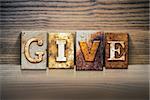 The word "GIVE" written in rusty metal letterpress type sitting on a wooden ledge background.