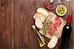 Prosciutto, wine, olives, parmesan and olive oil on wooden table. Top view with copy space