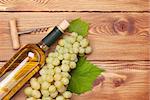 White wine bottle and bunch of white grapes on wooden table background with copy space