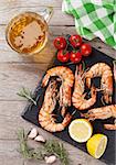 Grilled shrimps on stone plate and beer mug on wooden table