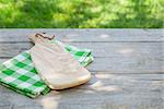 Empty wooden garden table with cutting board over tablecloth with green sunny bokeh background