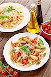 Spaghetti and penne pasta with tomatoes and basil on wooden table