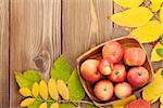 Apples in bowl and colorful autumn leaves on wooden background with copy space