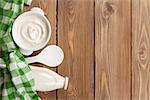 Sour cream in a bowl and milk bottle on wooden table. Top view with copy space