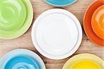 Colorful plates and saucers over wooden table background. View from above