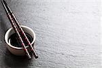 Japanese sushi chopsticks over soy sauce bowl on black stone background. Top view with copy space