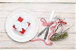 Gift box on plate, silverware and christmas decor. View from above over white wooden table background