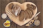 Healthy rye bread on a heart shaped board with wheat sheaths, yeast, oil, grain in lovespoon and scoop over oak background.