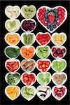 Healthy superfood vegetable and fruit selection in heart shaped porcelain dishes over black background, high in vitamins and antioxidants.
