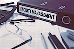 Facility Management - Office Folder on Background of Working Table with Stationery, Glasses, Reports. Business Concept on Blurred Background. Toned Image.