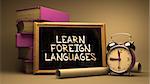 Learn Foreign Languages Handwritten on Chalkboard. Time Concept. Composition with Chalkboard and Stack of Books, Alarm Clock and Scrolls on Blurred Background. Toned Image.