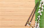 Chopsticks and sakura branch over bamboo mat with copy space
