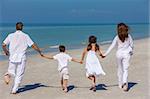 Rear view of happy family of mother, father and two children, son and daughter, running holding hands and having fun in the sand of a sunny beach
