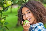 Outdoor portrait of beautiful happy mixed race African American girl teenager female child eating an organic green apple and smiling with perfect teeth