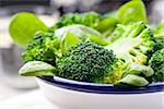 Broccoli, baby spinach and green beans salad in ceramic bowl with olive oil on a white wooden background.