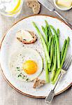 Green asparagus with fried egg and bread with butter on a white plate.