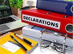 Red Ring Binder with Inscription Declarations on Background of Working Table with Office Supplies, Laptop, Reports. Toned Illustration. Business Concept on Blurred Background.