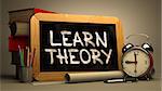 Learn Theory Handwritten by white Chalk on a Blackboard. Composition with Small Chalkboard and Stack of Books, Alarm Clock and Rolls of Paper on Blurred Background. Toned Image.