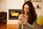 Beautiful woman using a cellphone at home at the warmth of a fireplace