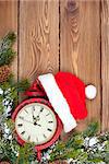 Christmas wooden background with clock, snow fir tree and santa hat