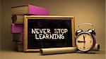 Never Stop Learning Handwritten by white Chalk on a Blackboard. Composition with Small Chalkboard and Stack of Books, Alarm Clock and Rolls of Paper on Blurred Background. Toned Image.