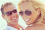 Instagram style photograph of happy and attractive man and woman couple wearing sunglasses and smiling in sunshine at the beach