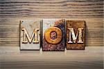 The word "MOM" written in rusty metal letterpress type sitting on a wooden ledge background.