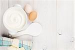 Sour cream in a bowl and eggs on wooden table. Top view with copy space