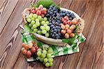 Bunch of red, purple and white grapes in basket on wooden table background