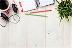 Office wooden desk with notepad, coffee cup and headphones. Top view with copy space