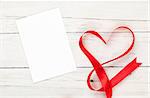 Photo frame or gift card with valentines heart shaped ribbon over wooden table background