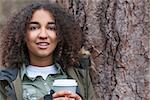 Beautiful happy mixed race African American girl teenager female young woman smiling and drinking takeaway coffee outside next to a tree