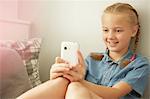 Girl sitting leaning against wall looking at smartphone smiling