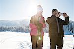 Senior couple on snowy landscape using smartphone to take photograph, Sattelbergalm, Tyrol, Austria