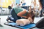 College student performing CPR on mannequin in class