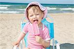 Female toddler wearing sunhat eating ice lolly on beach chair