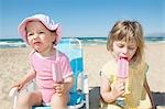 Female toddler and sister eating ice lollies on beach