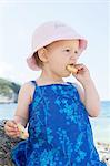 Female toddler wearing sunhat eating doughnut on beach