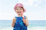 Female toddler wearing sunhat eating ice lolly on beach