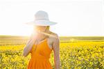 Mid adult woman using mobile phone in canola field wearing sunhat looking down