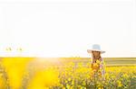 Mid adult woman in canola field wearing sunhat looking down, focus on background