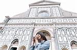 Low angle view of young woman using digital camera in front of church, Piazza Santa Maria Novella, Florence, Tuscany, Italy