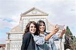 Lesbian couple using smartphone to take selfie in front of church, Piazza Santa Maria Novella, Florence, Tuscany, Italy