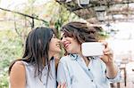 Lesbian couple in plant covered archway using smartphone to take selfie,face to face, Florence, Tuscany, Italy