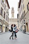 Low angle view of lesbian couple standing in street below the Palazzo Vecchio face to face hugging, Florence, Tuscany, Italy