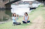 Lesbian couple sitting on arno river bank in front of Ponte Vecchio holding digital camera smiling, Florence, Tuscany, Italy