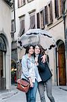 Lesbian couple standing together in street holding umbrella looking at camera smiling, Florence, Tuscany, Italy