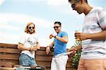 Three male friends drinking beer and barbecuing at rooftop barbecue